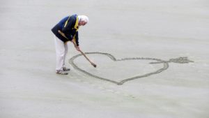 old lady drawing a heart in the sand