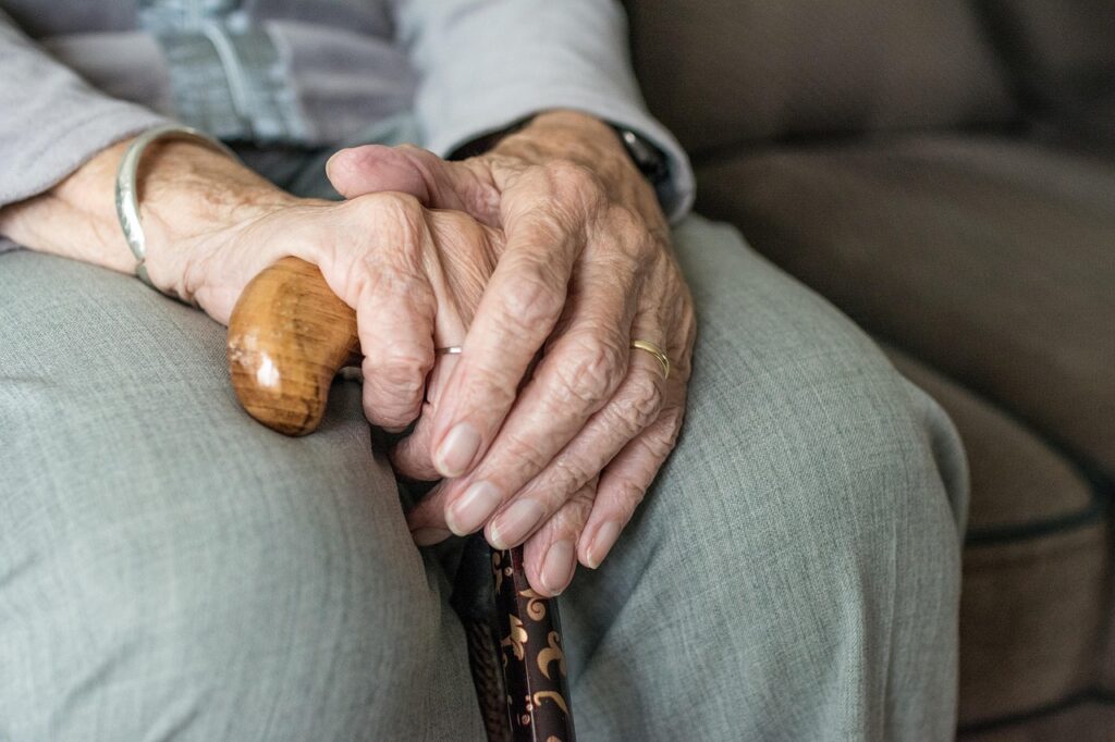 Senior hands resting on a cane while seated on a couch, preparing to use the cane for support